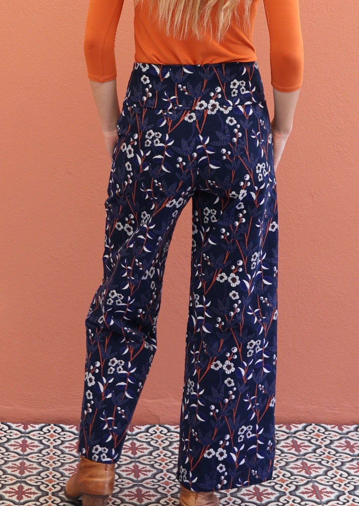 Back pose of model in printed cotton corduroy pants with wide waistband and pockets.