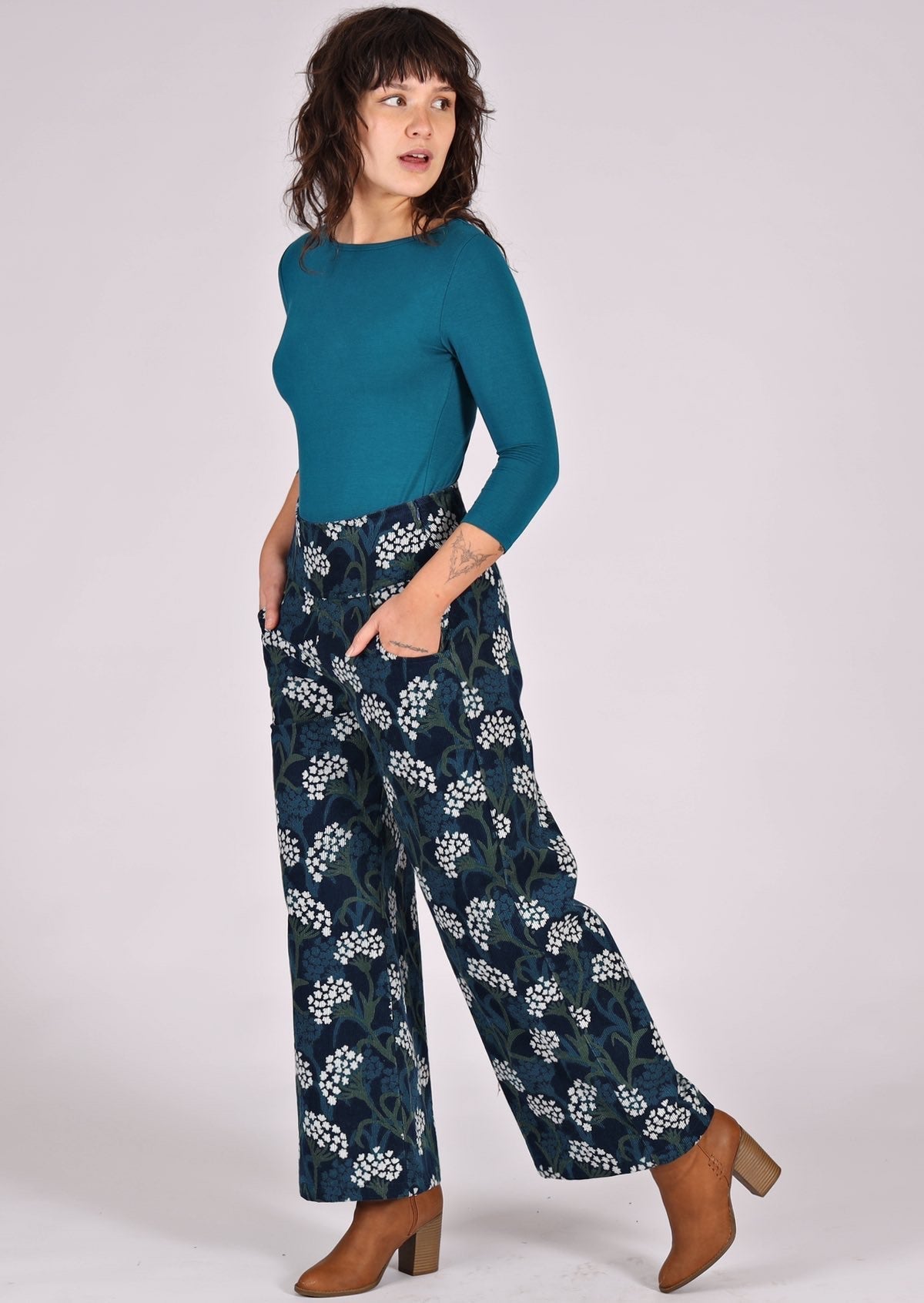 Model poses in blue, green and white floral print on dark blue base cotton corduroy pants, paired with teal stretch top