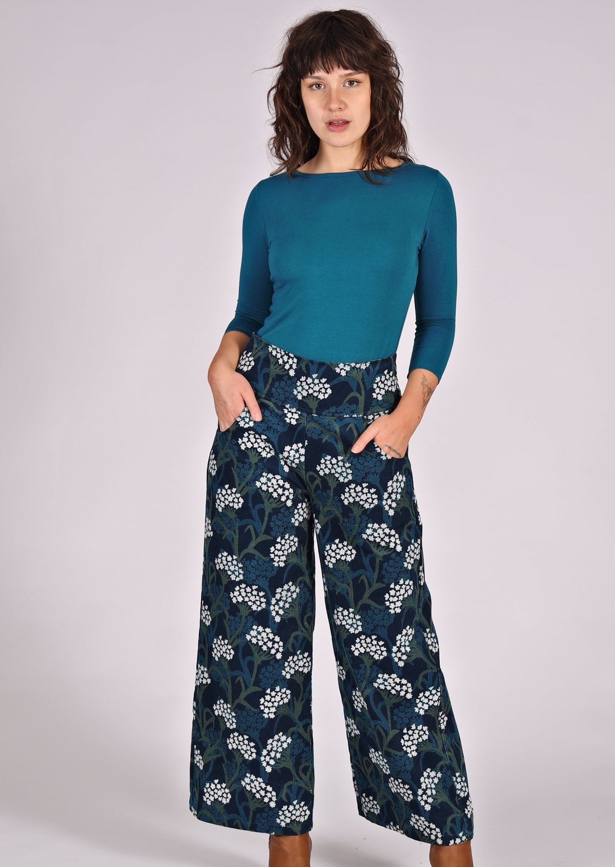 Woman wears blue, green and white floral print on dark blue base cotton corduroy pants with hands in pockets
