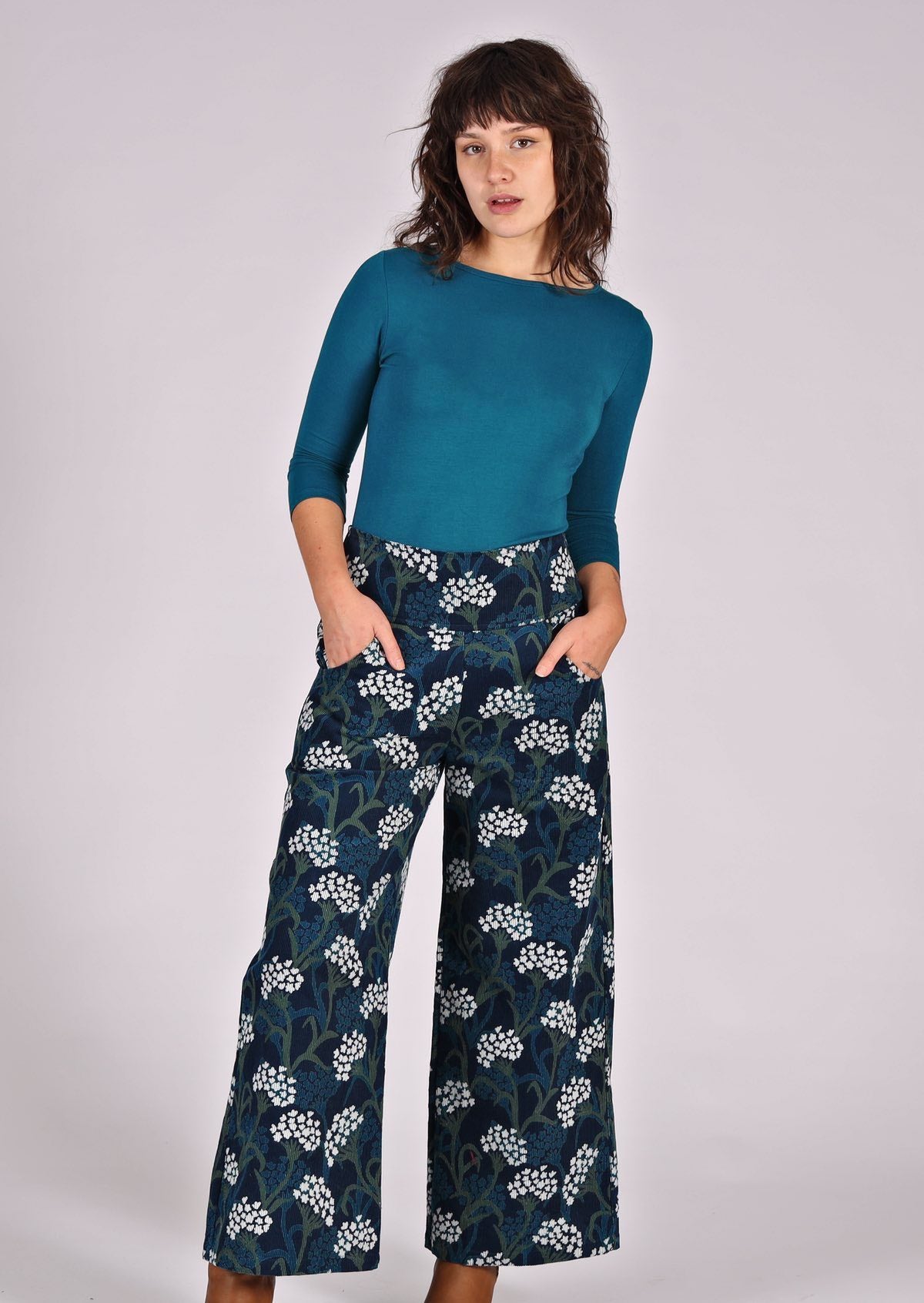 Model poses in blue, green and white floral print on dark blue base cotton corduroy pants with hands in pockets