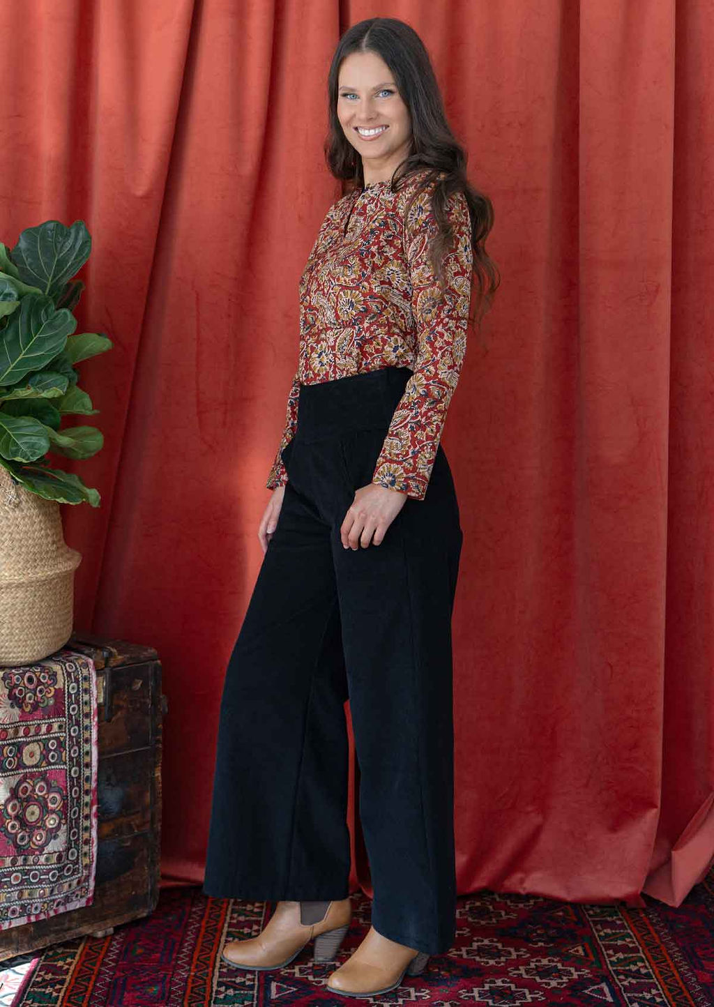 woman wearing black corduroy wide leg pants with hand on hip, paired cotton blouse top and ankle boots