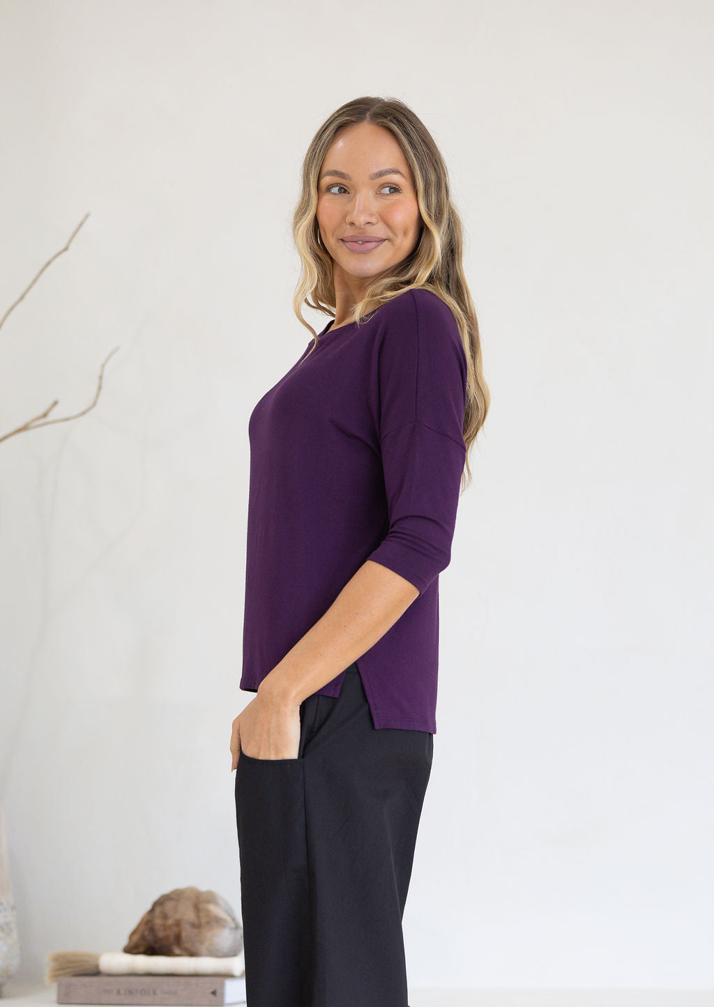 Woman stands side on wearing a stretch rayon purple relaxed fit top and black pants