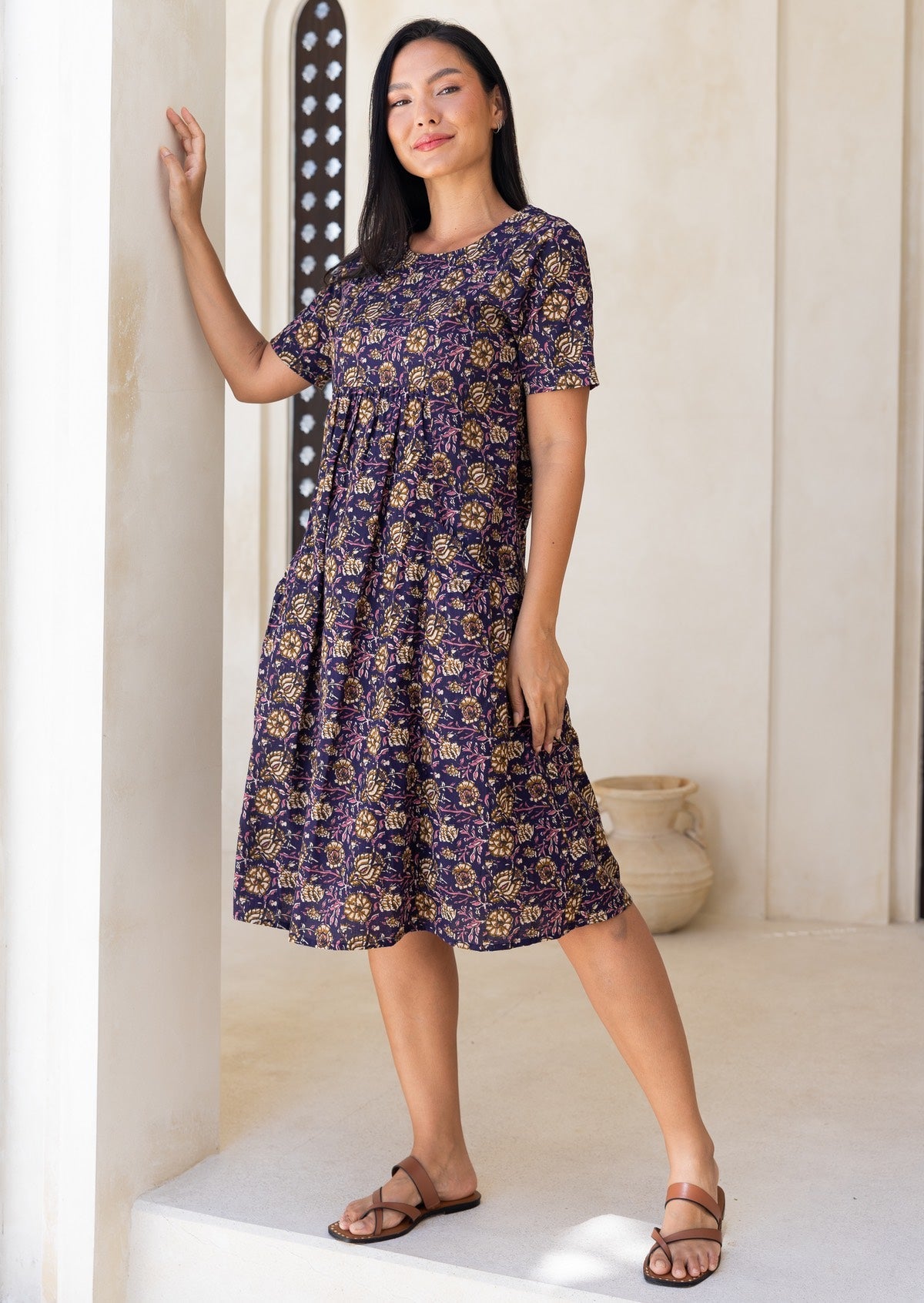 Woman wearing a purple cotton floral sun dress standing in a bright, light room.