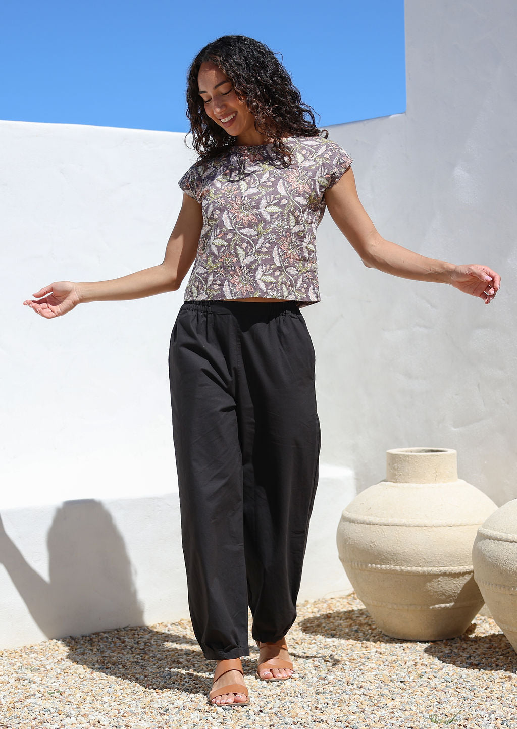 Model poses in high waisted wide leg cotton pants in black with elastic waist, pockets and pleated ankles