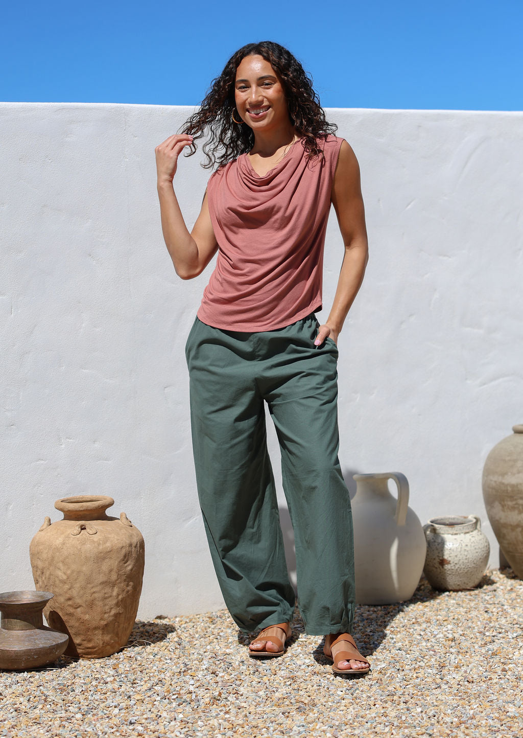 Woman wearing a pink sleeveless top and green relaxed fit pants standing with hand in pocket