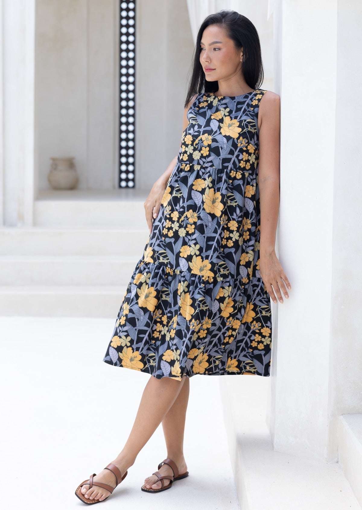 Woman standing against the white wall is wearing tiered midi length dress with relaxed fit, empire waist and pockets gorgeous black based floral print