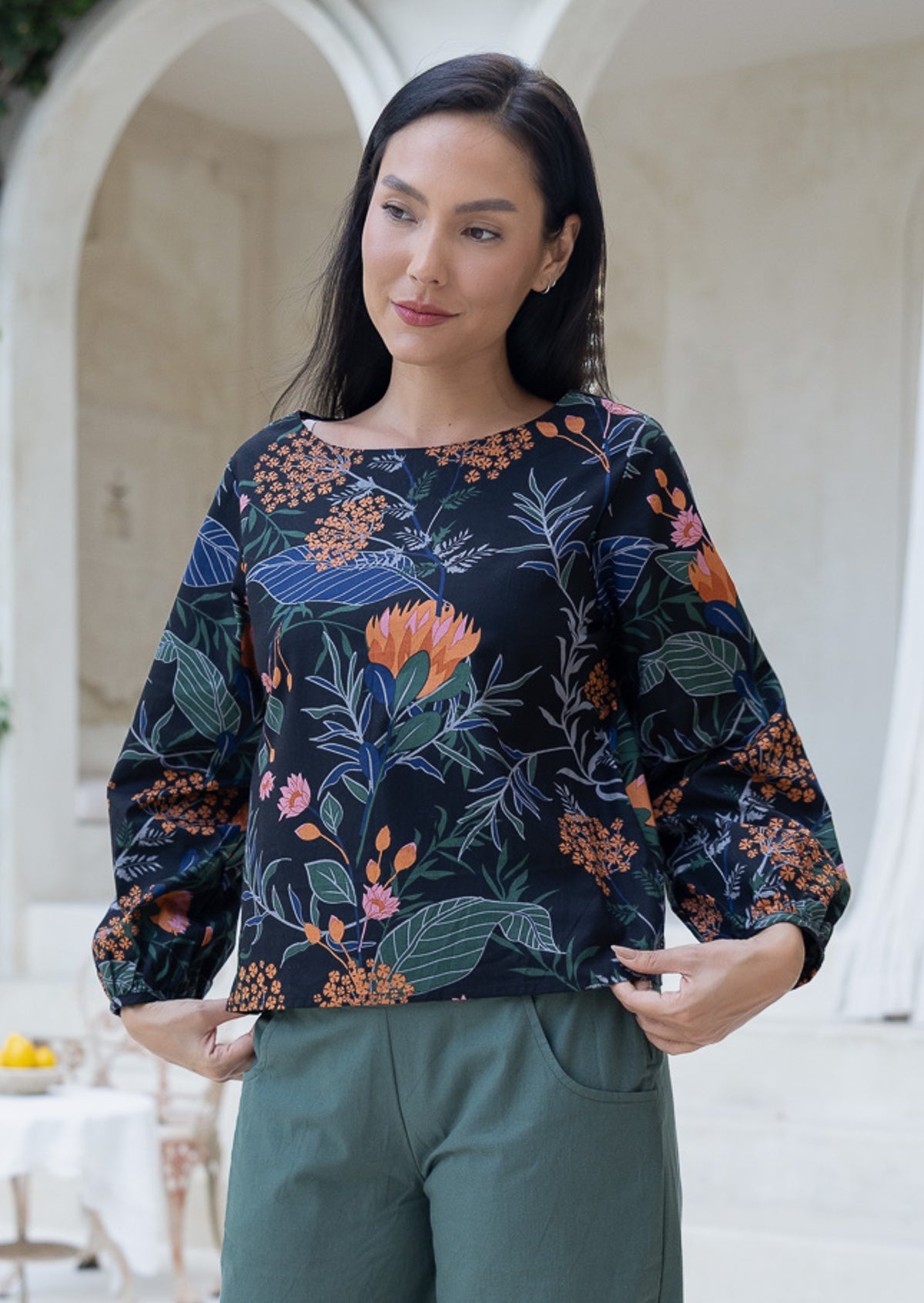 Model wears cotton bishop sleeved top with wide round neckline, black based queen protea print featuring pink and orange florals