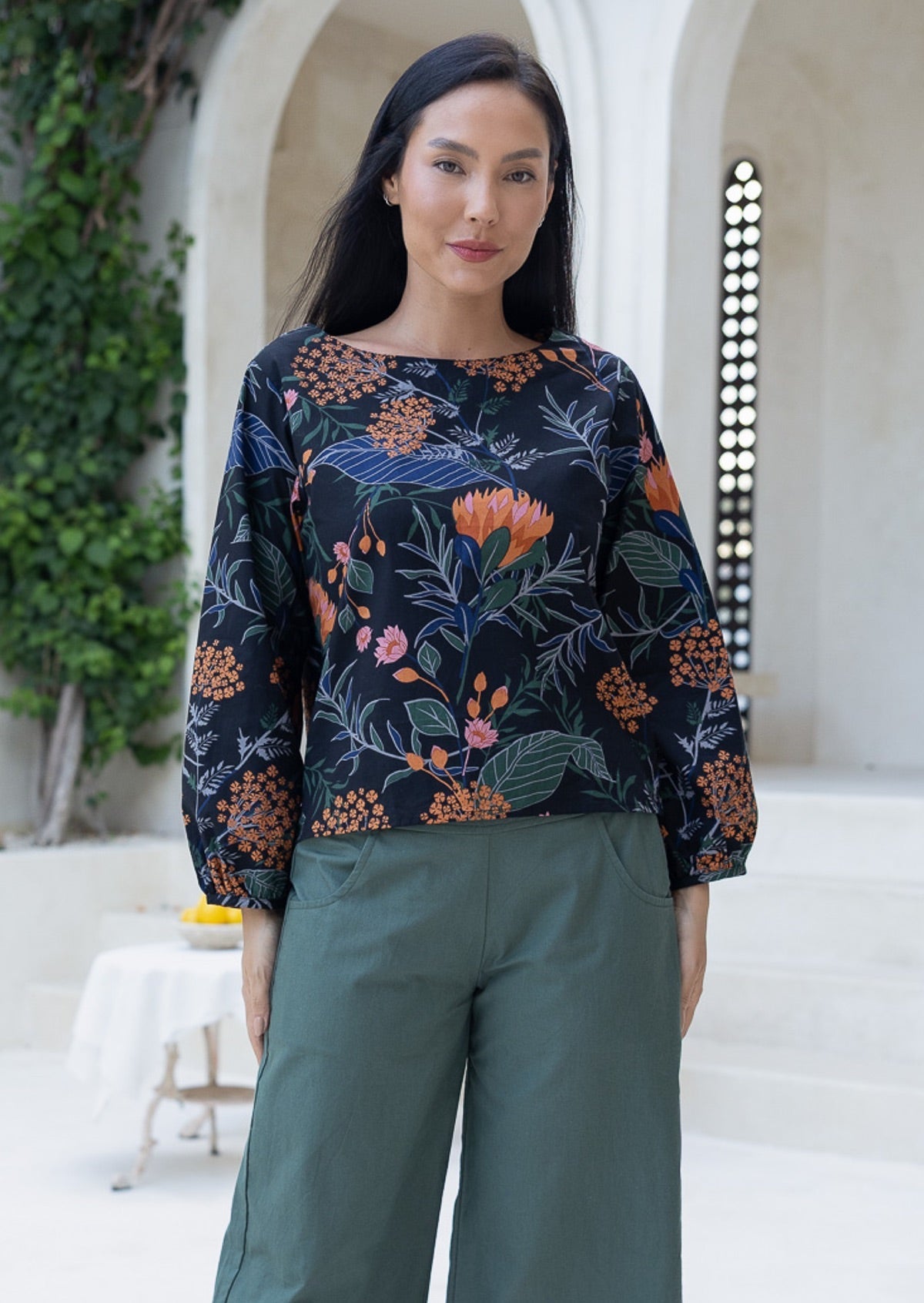 Woman wearing a 100% cotton botanical print top in black and green pants in an outdoor setting