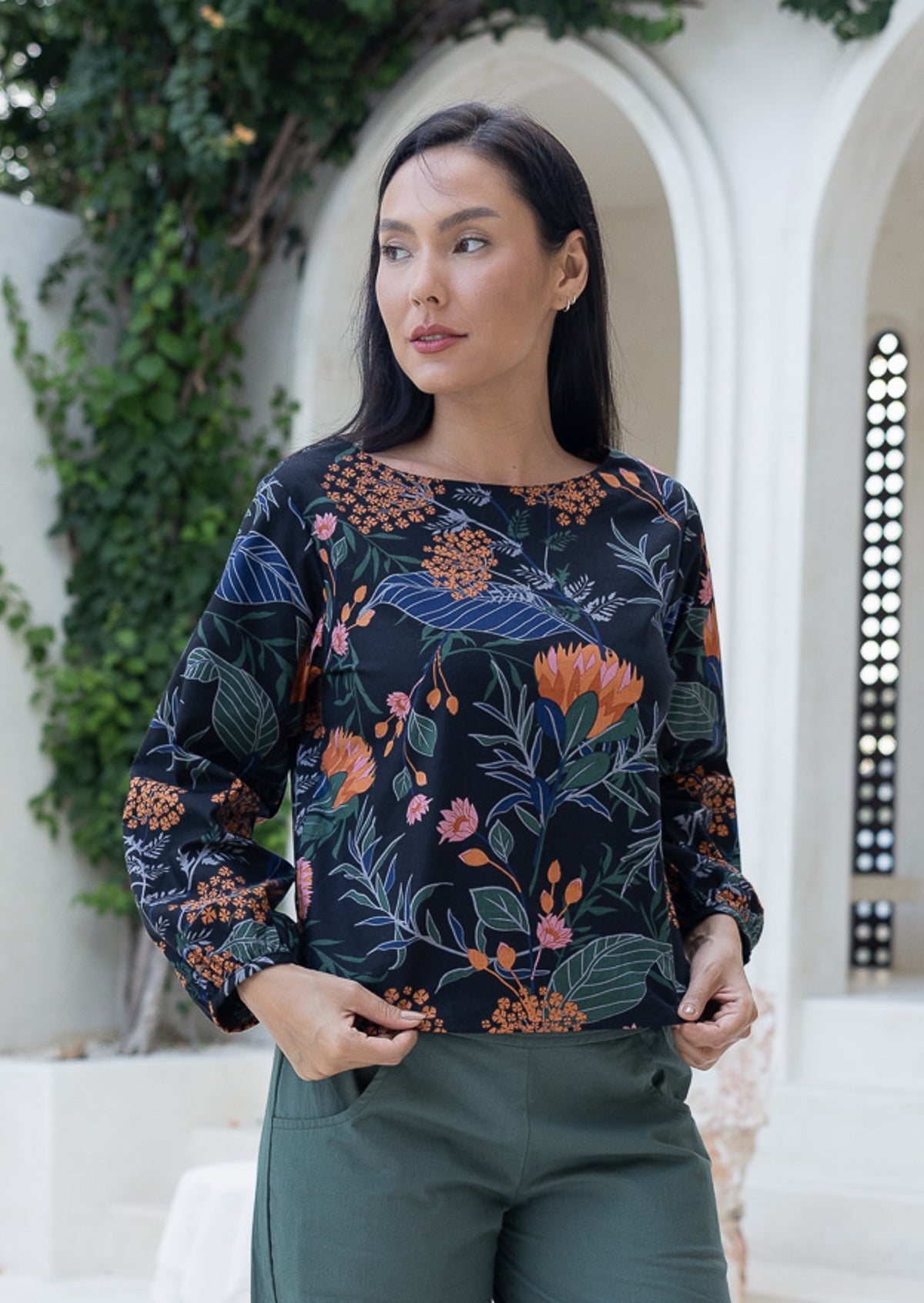 Woman wearing a dark floral cotton top with long bishop sleeves and boat neckline