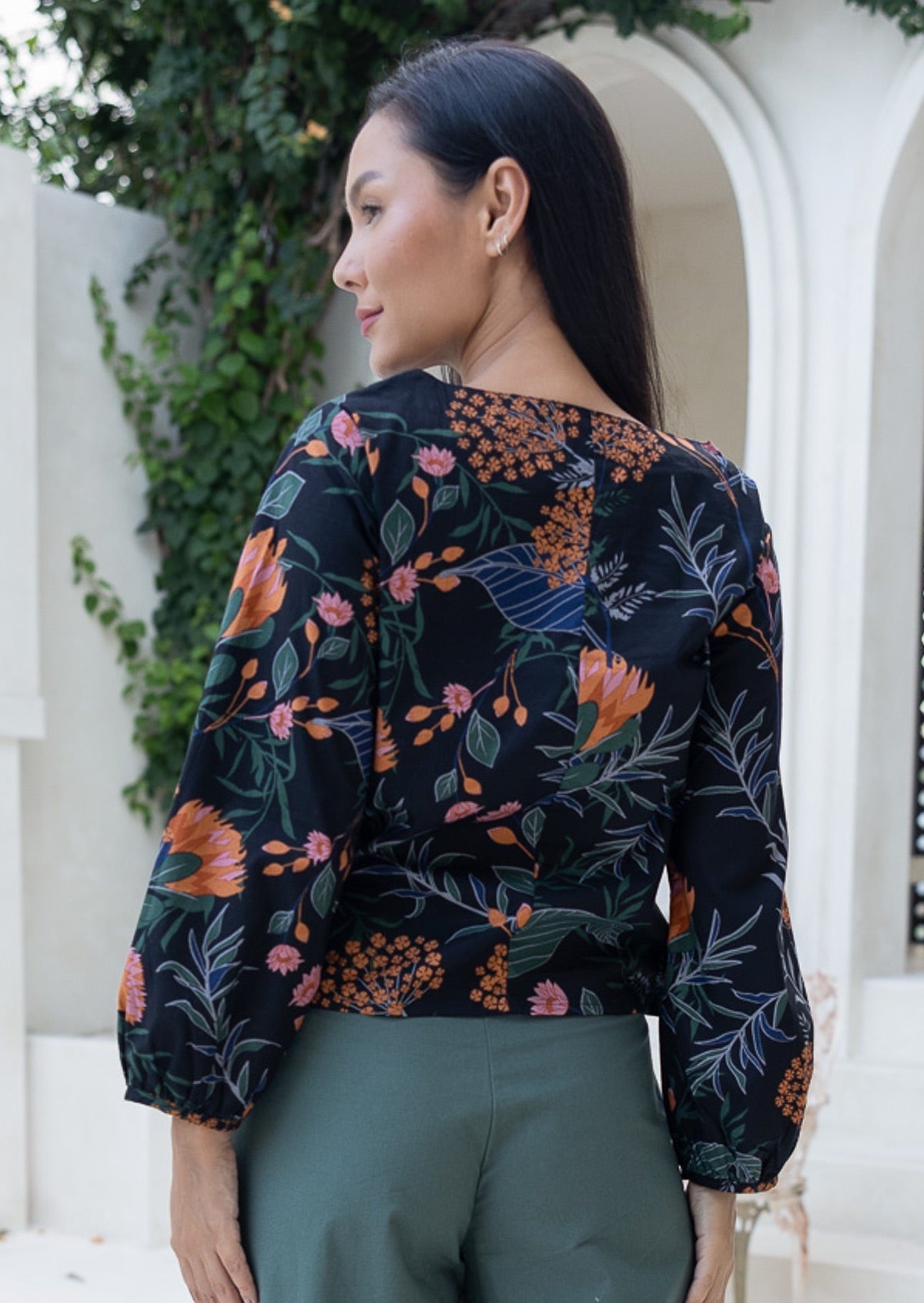 Back view of woman wearing a beautiful botanic print black cotton top with bishop sleeves and vertical center back seam.