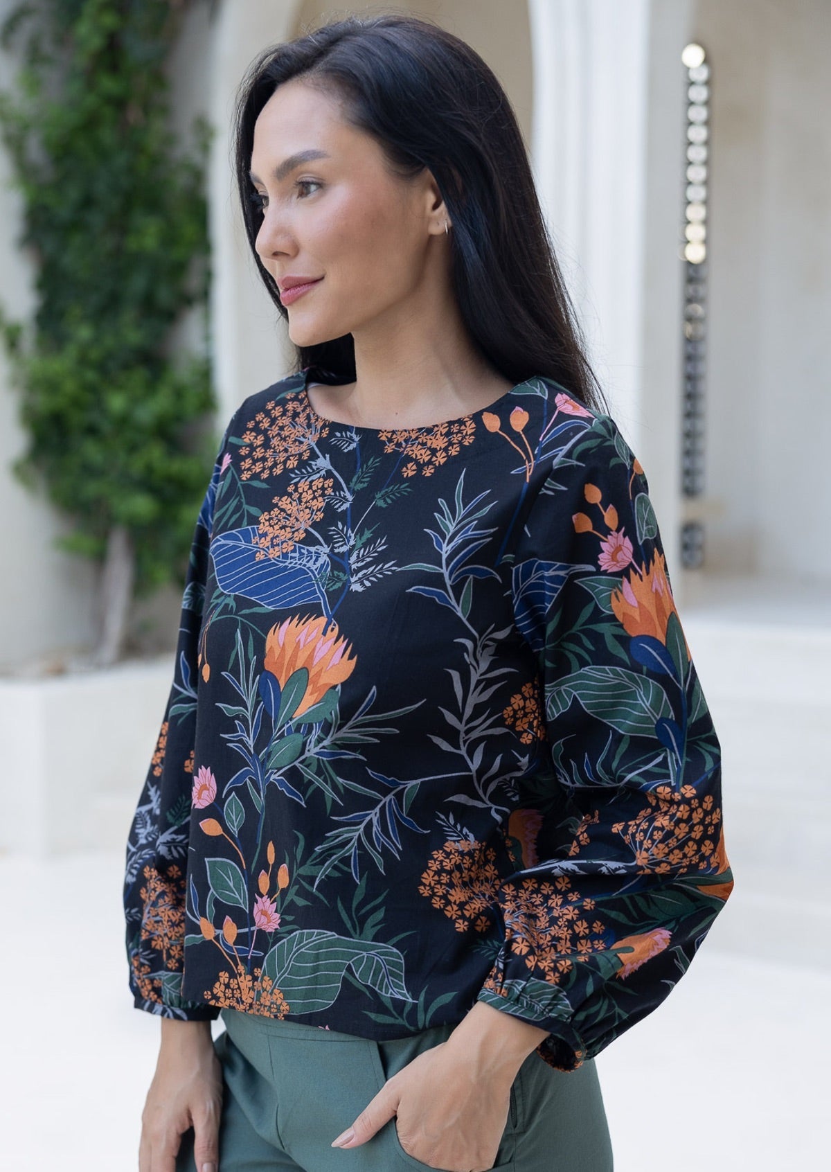 Woman wearing a black 100% cotton top with bishop sleeves and boat neckline in beautiful queen protea print