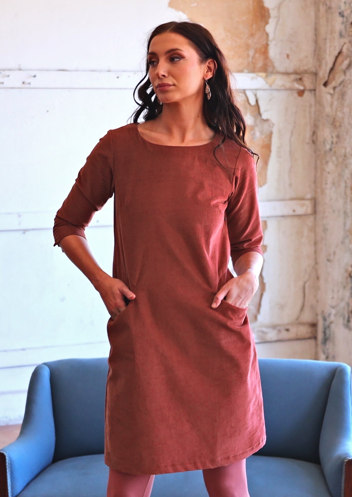 Woman in long sleeve rust coloured corduroy tunic with hands in pocket