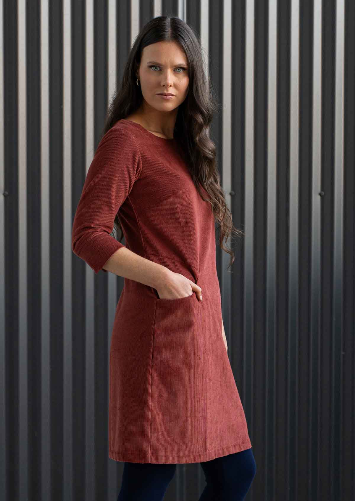 Woman wearing rust coloured corduroy tunic with sleeves over navy blue leggings with hands in pockets