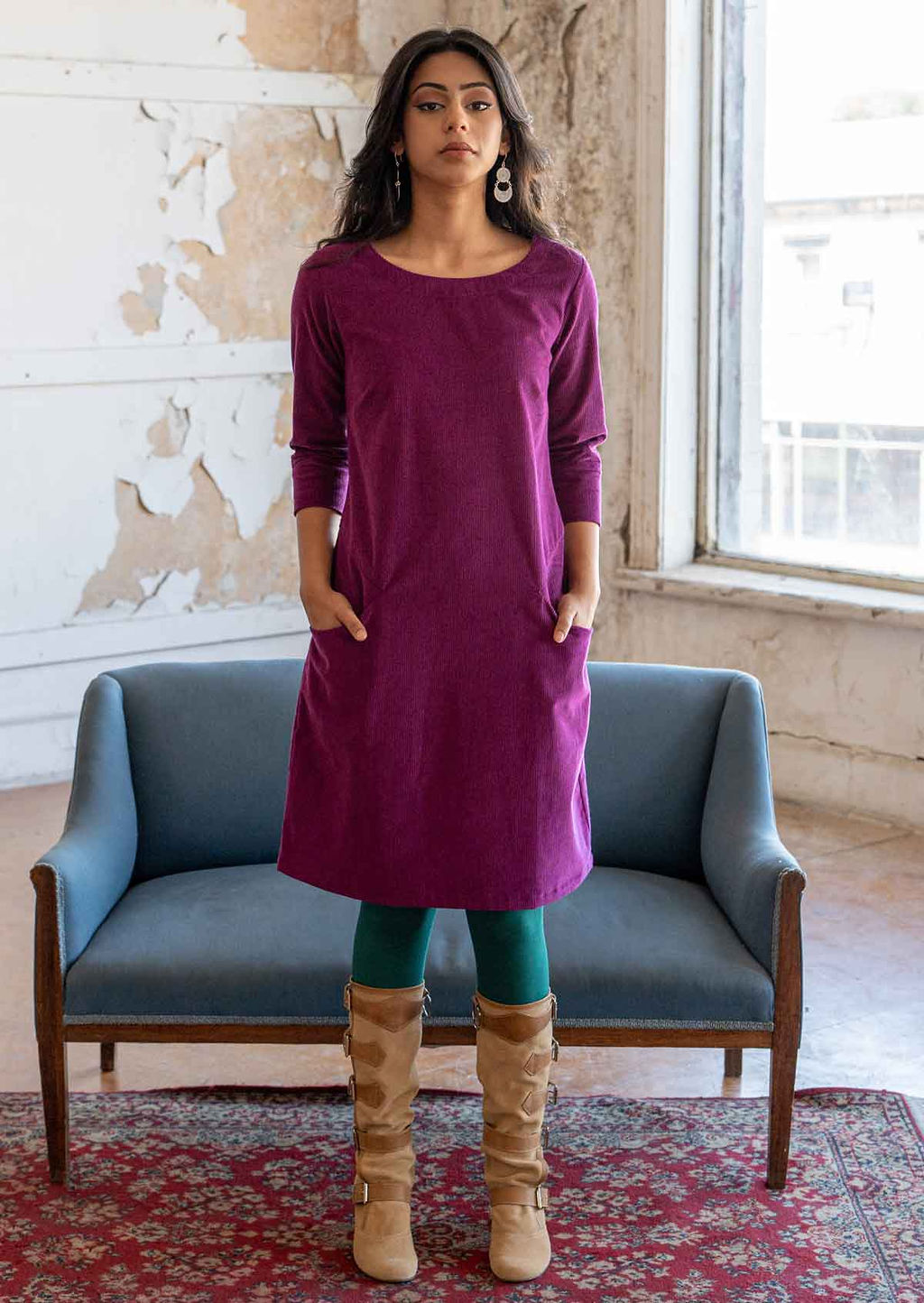 Woman standing in front of blue couch wearing 100% cotton 3/4 sleeve corduroy shift dress with hands in pockets