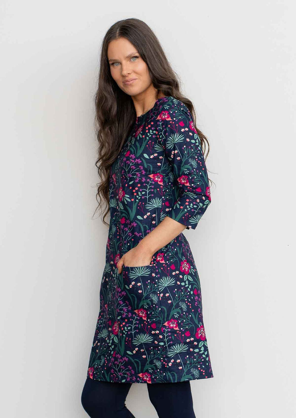 Woman leaning against wall wearing Cotton 3/4 sleeve shift dress with detailed cuff, in gorgeous floral print on dark blue base