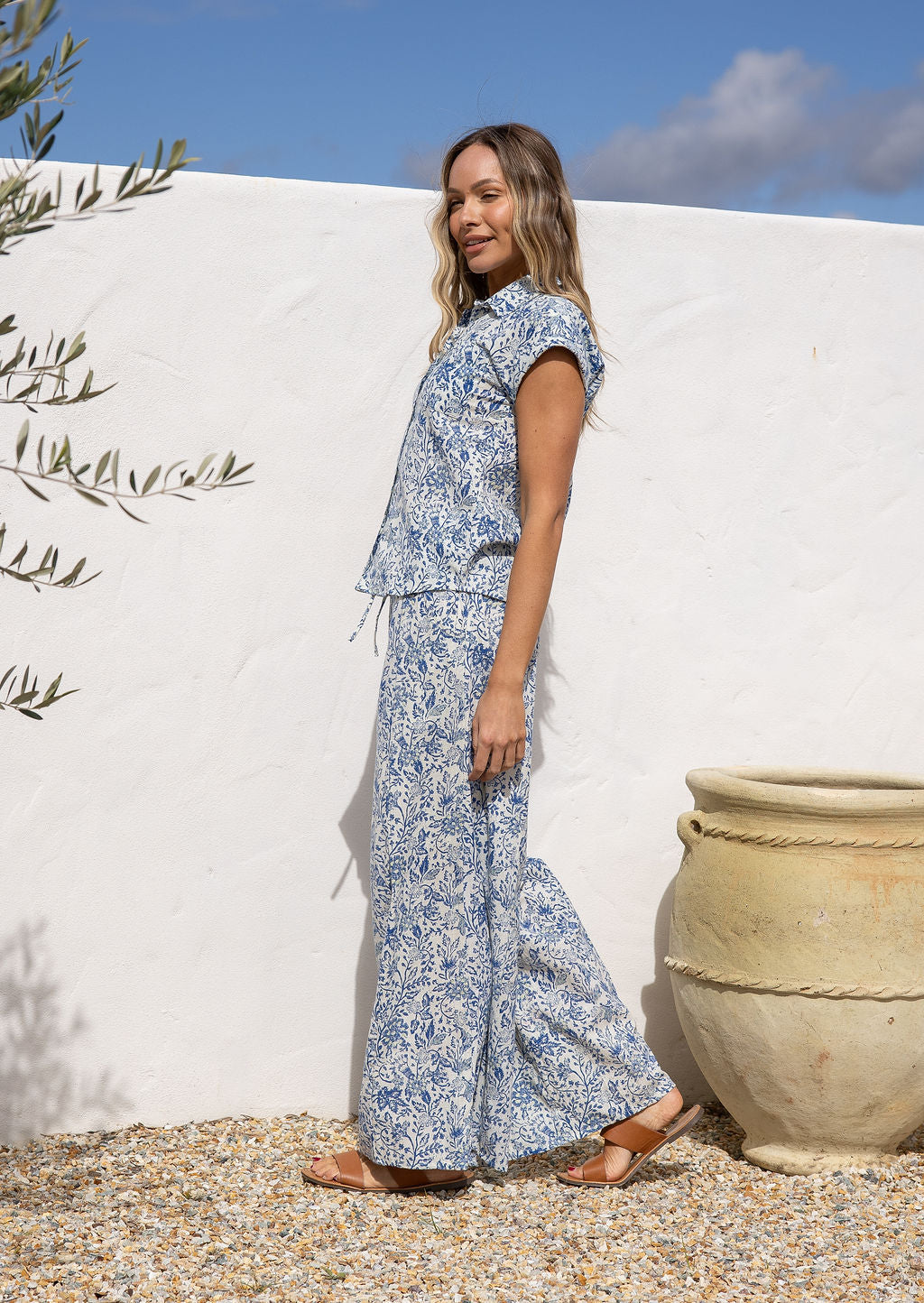 Woman in a white based blue floral cotton pant against a white wall.