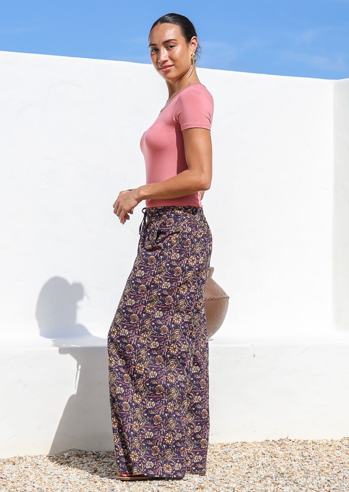 Side pose of model wearing wide leg, floral printed cotton pants with pockets and elastic waist at the back.