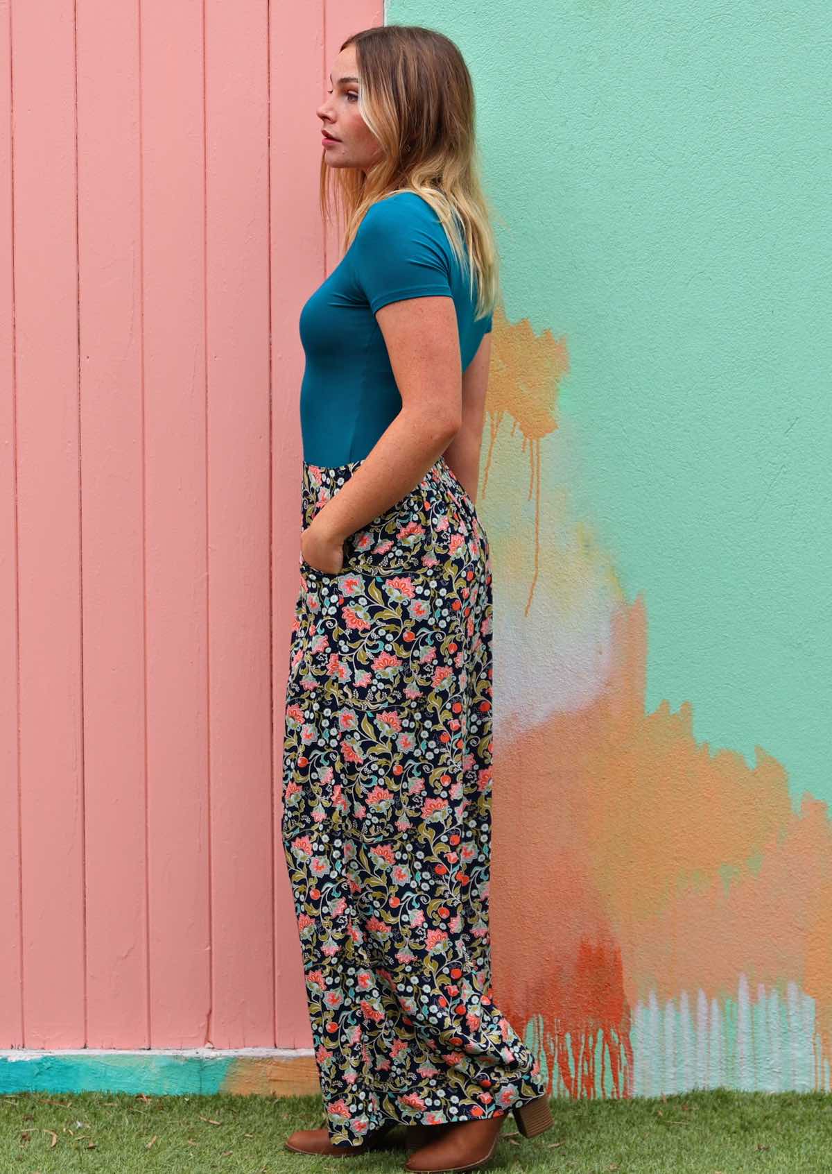 Model stands sideways in wide leg floral print rayon pants with hand in pocket
