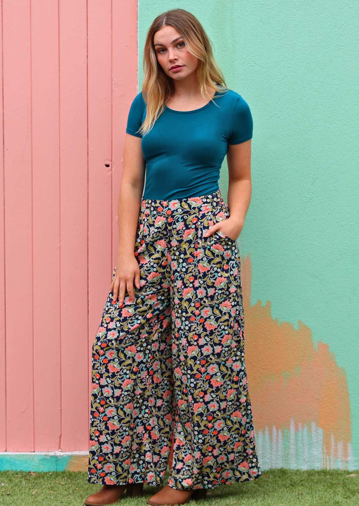 Woman poses in high waisted wide leg floral print rayon pants with hand in pocket