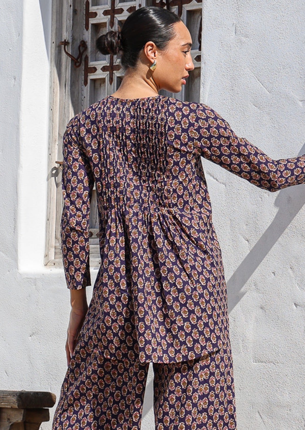 Woman wears cotton long sleeve top with longer back and small pin tucks across front and back of bodice.