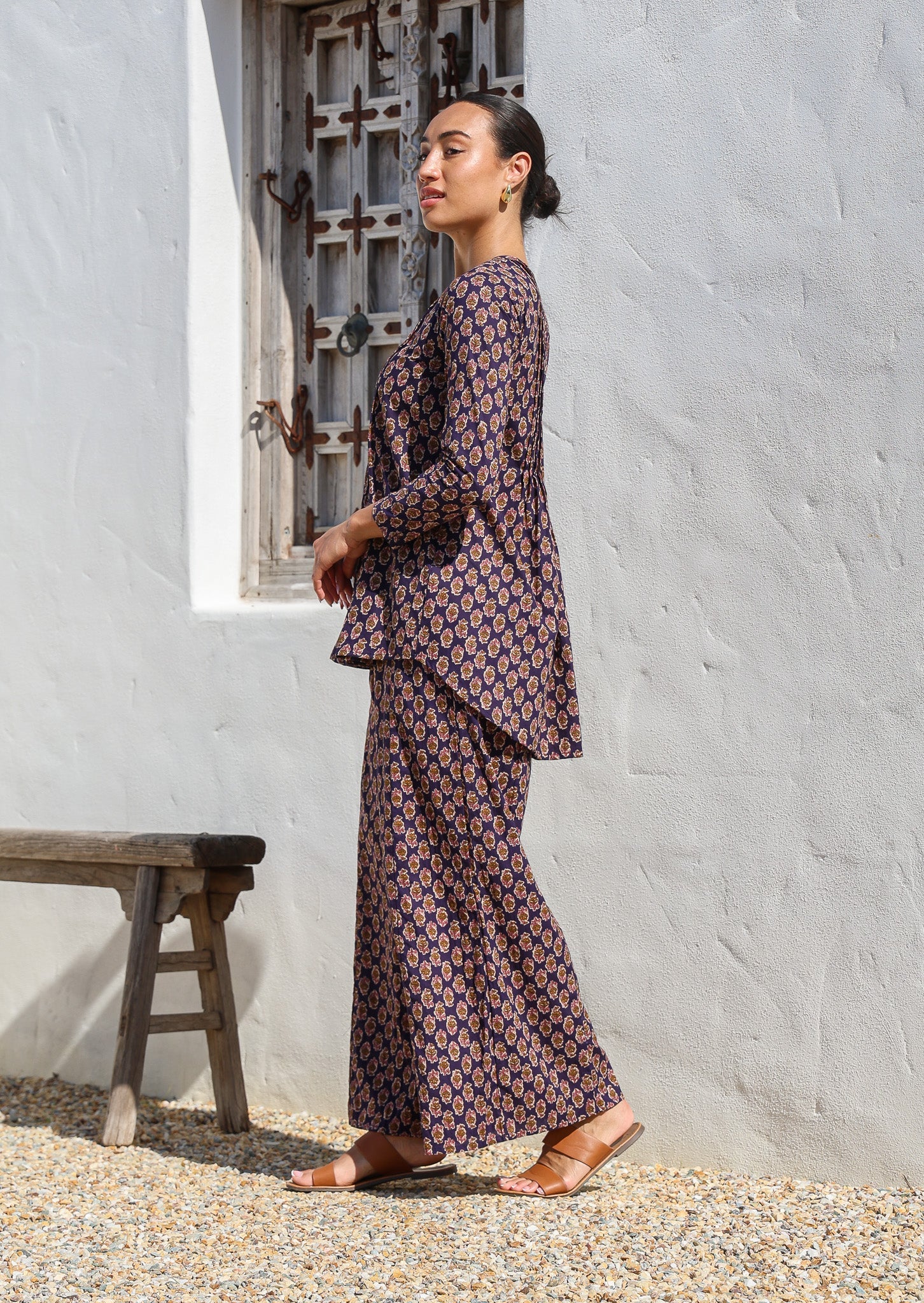 Side pose of model wearing cotton long sleeve, button through top in dark purple with wide leg, floral printed pants.