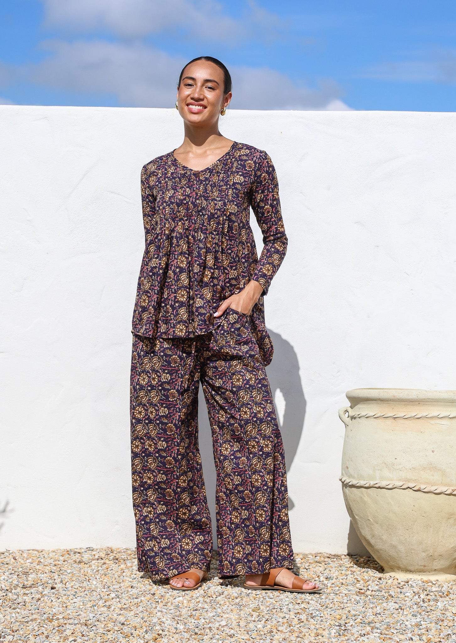 Model poses in long sleeve button through top with V-neckline and small pin-tucks across chest that leads into flared base