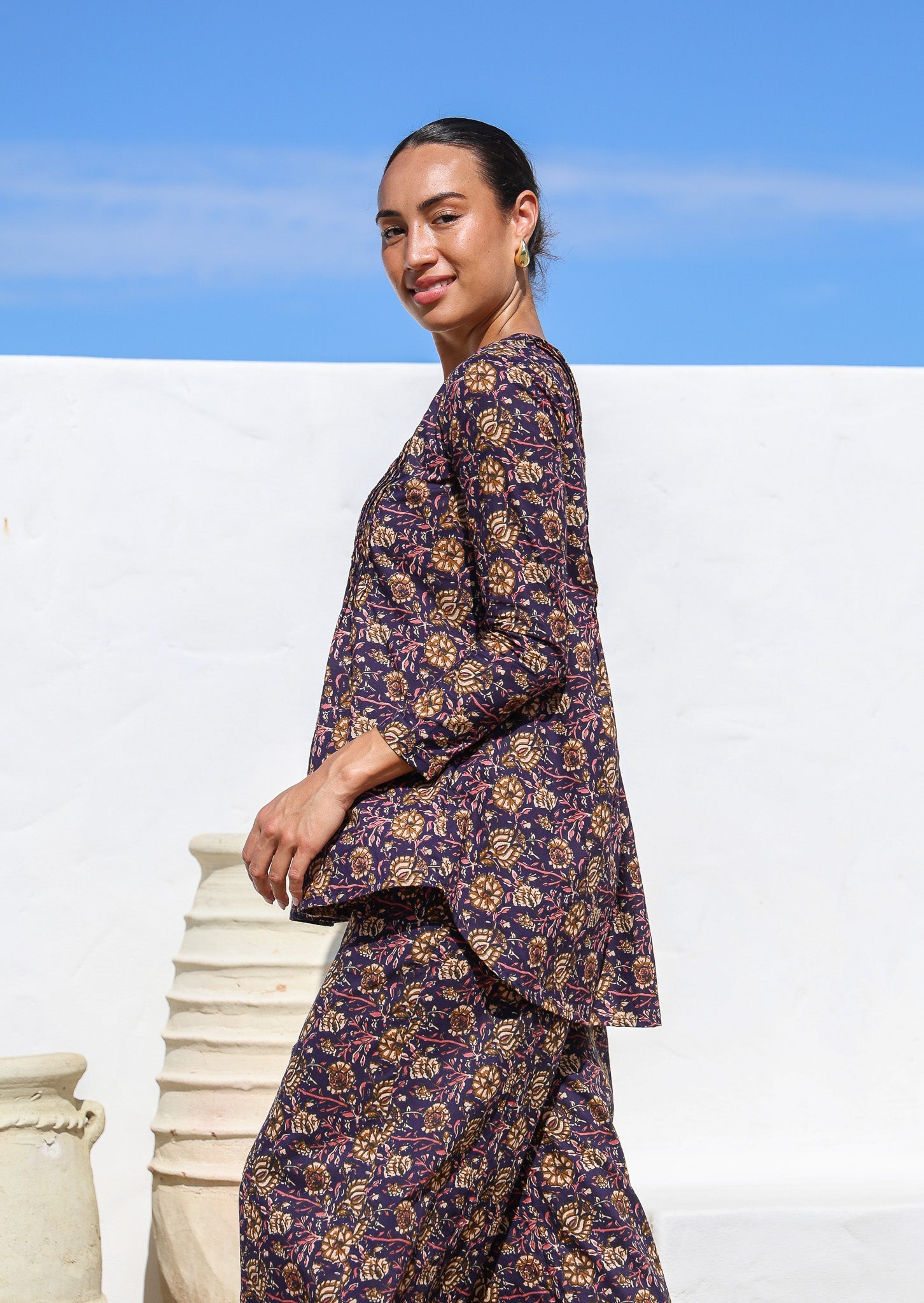 Model standing sideways wears 100% cotton long sleeve top in dark purple with pintucks at the back and front.