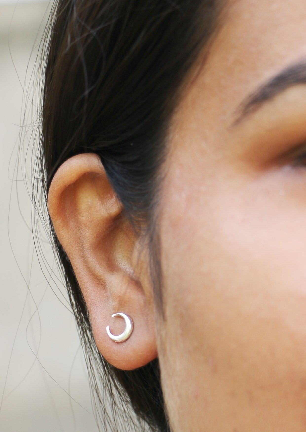 Close-up of a woman's ear wearing a crescent moon luna love studs with blurred background