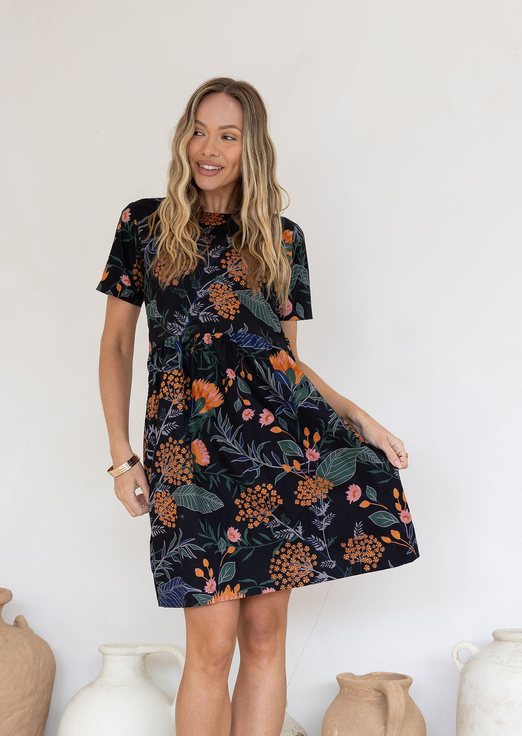Woman poses in loose fitting gorgeous black based cotton dress with blue, grey and green leafs and orange, pink florals.