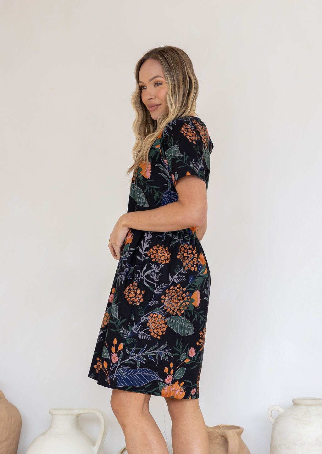 Model posing on sides in 100 percent cotton above knee length dress with high round neckline, short sleeves and pockets.