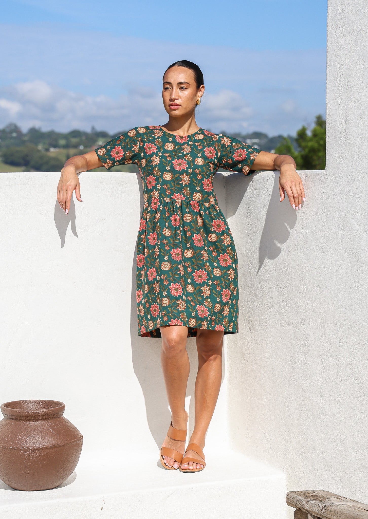 Model standing with relaxed hands in green short sleeved cotton dress with round neckline and hidden side pockets.