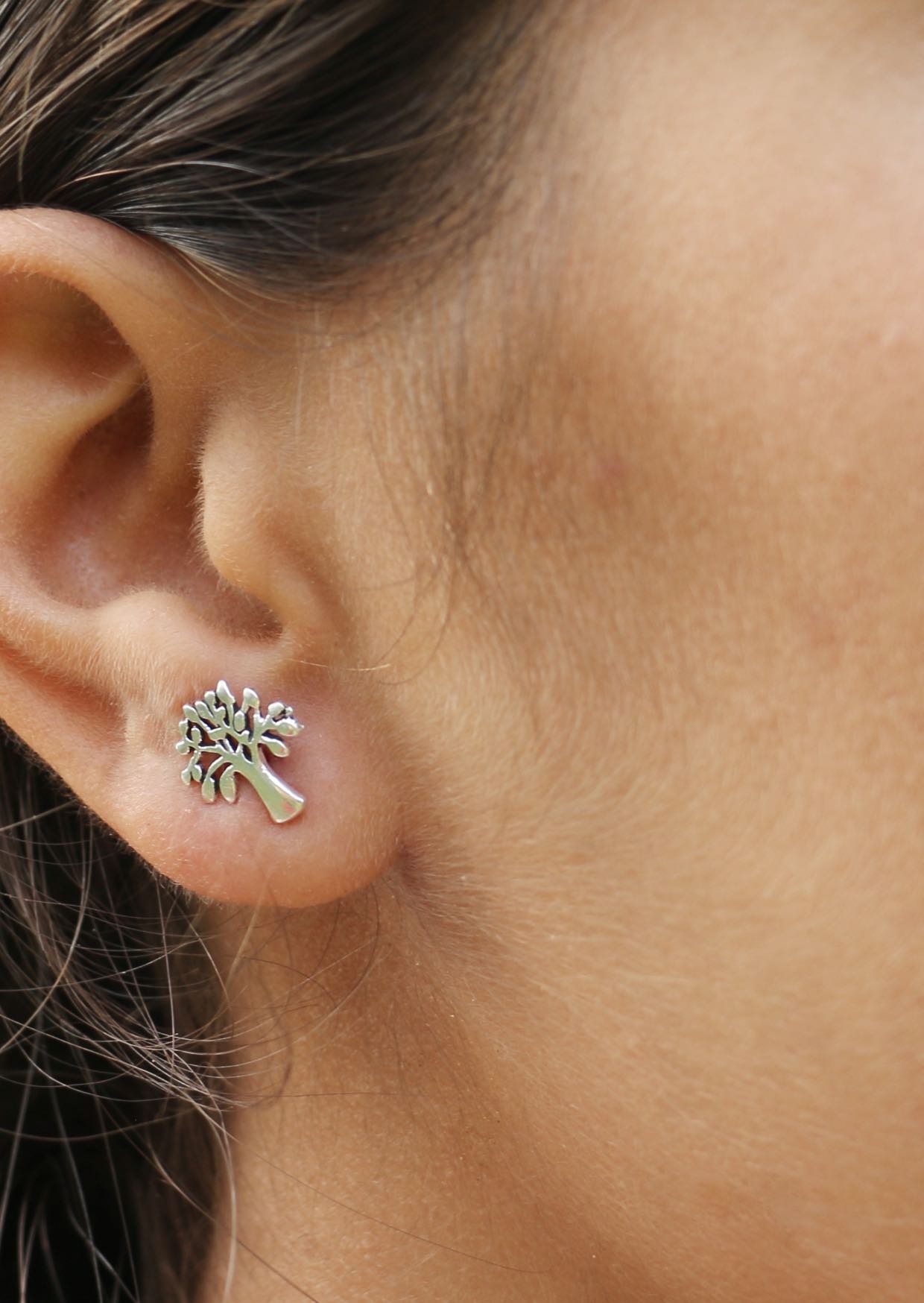 Close-up of an ear wearing a silver mango tree-shaped stud having butterfly back