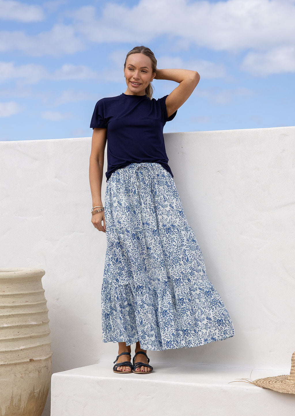 Woman wearing a white based blue floral cotton skirt standing against a white wall.