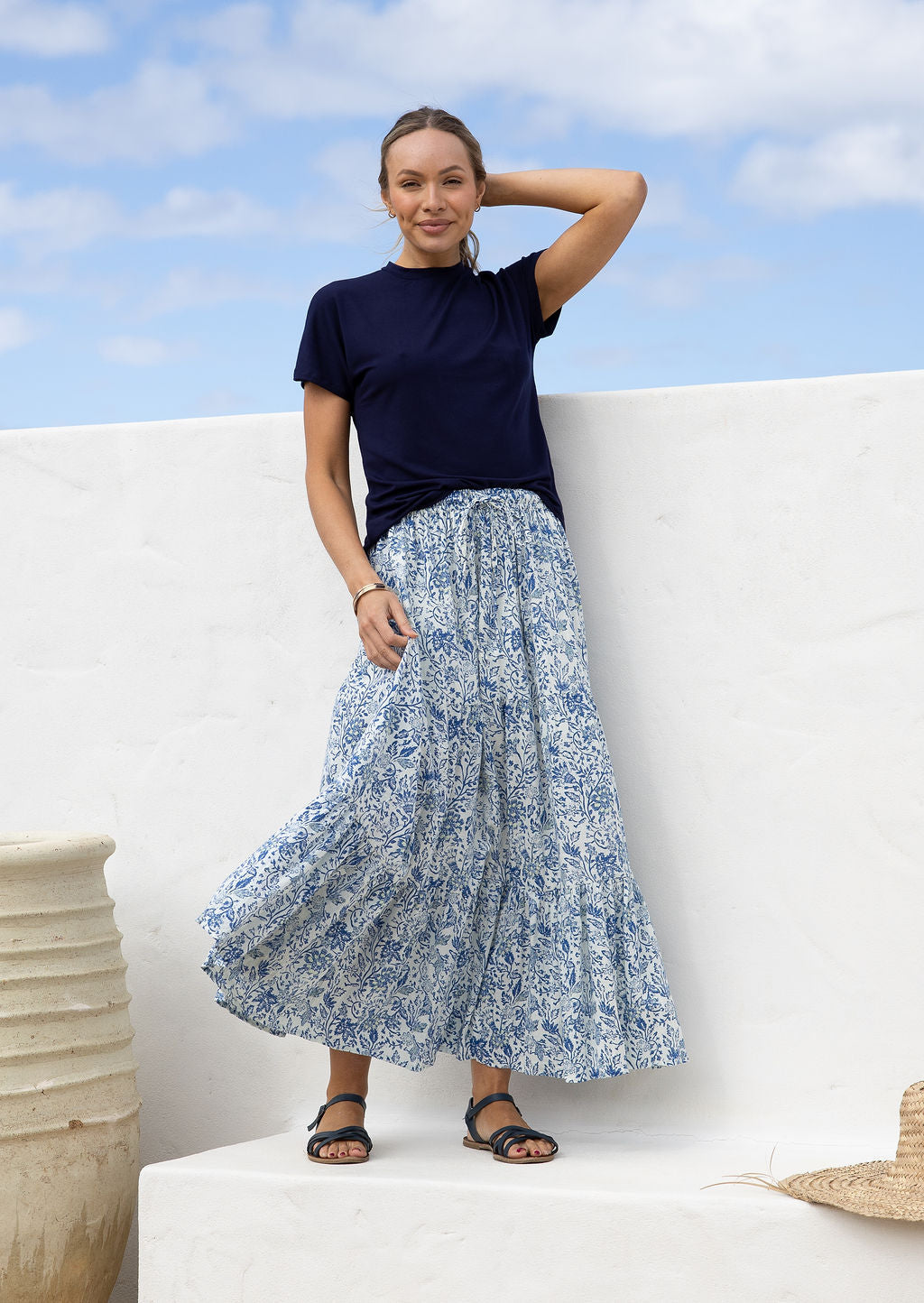 Woman wearing a white based blue floral cotton skirt standing against a white wall.
