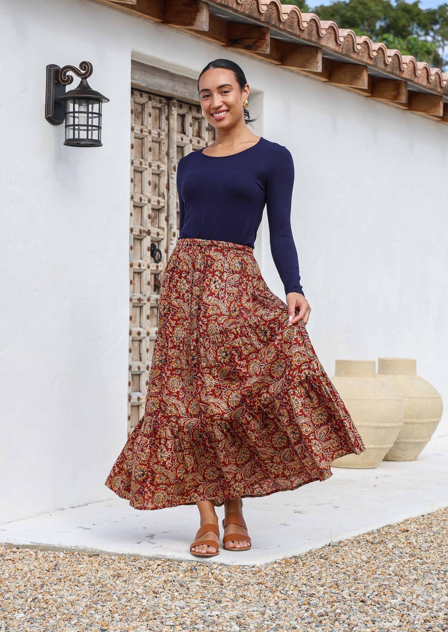 Model wears 100% cotton tiered maxi skirt with earthy floral print on rust base.