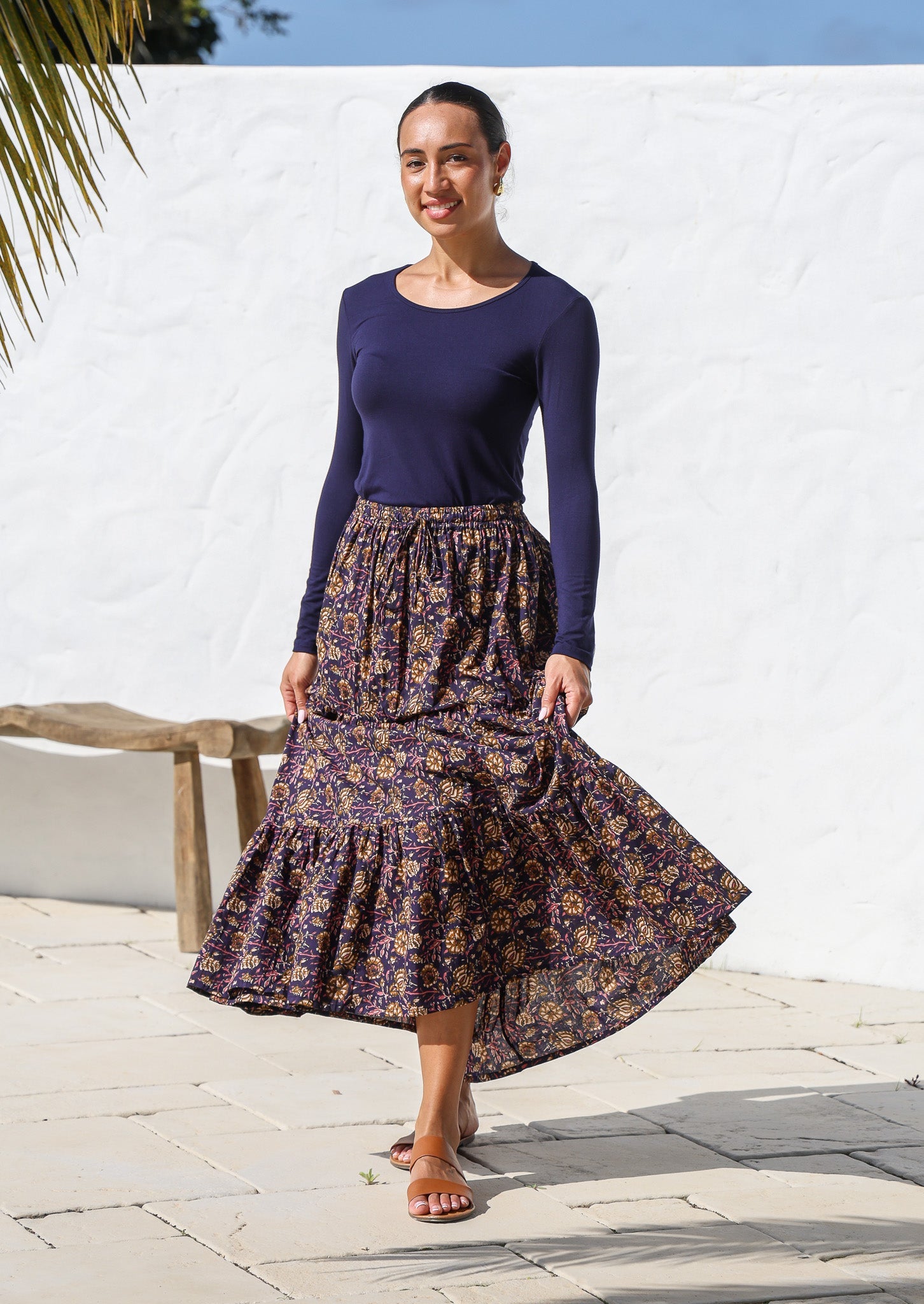 Model posing in a flowy cotton maxi skirt in dark purple based floral print, paired with long sleeve stretch top in navy blue.