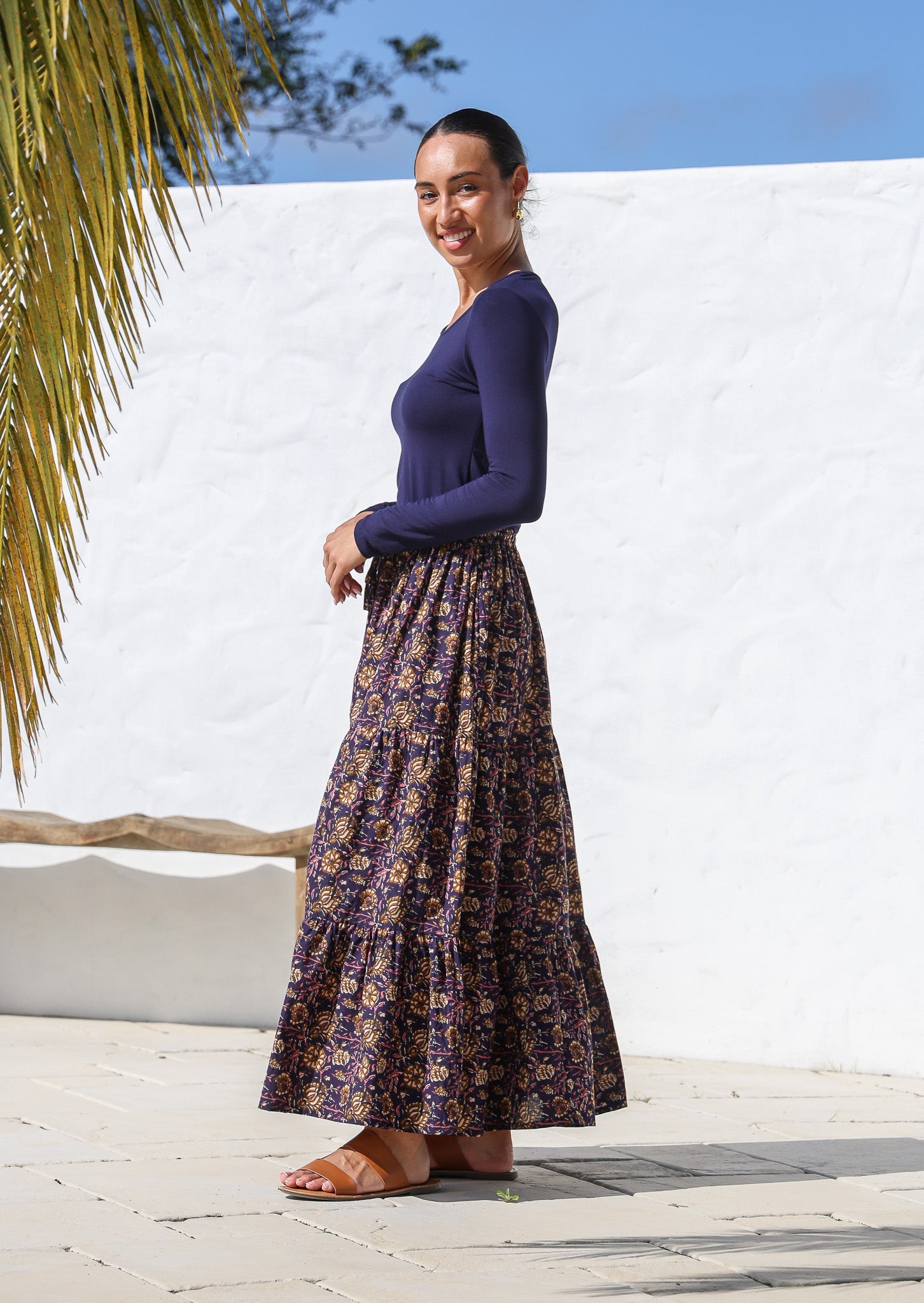 Model standing sideways wears a floral printed cotton maxi skirt with elasticated waist and shoestring tie.