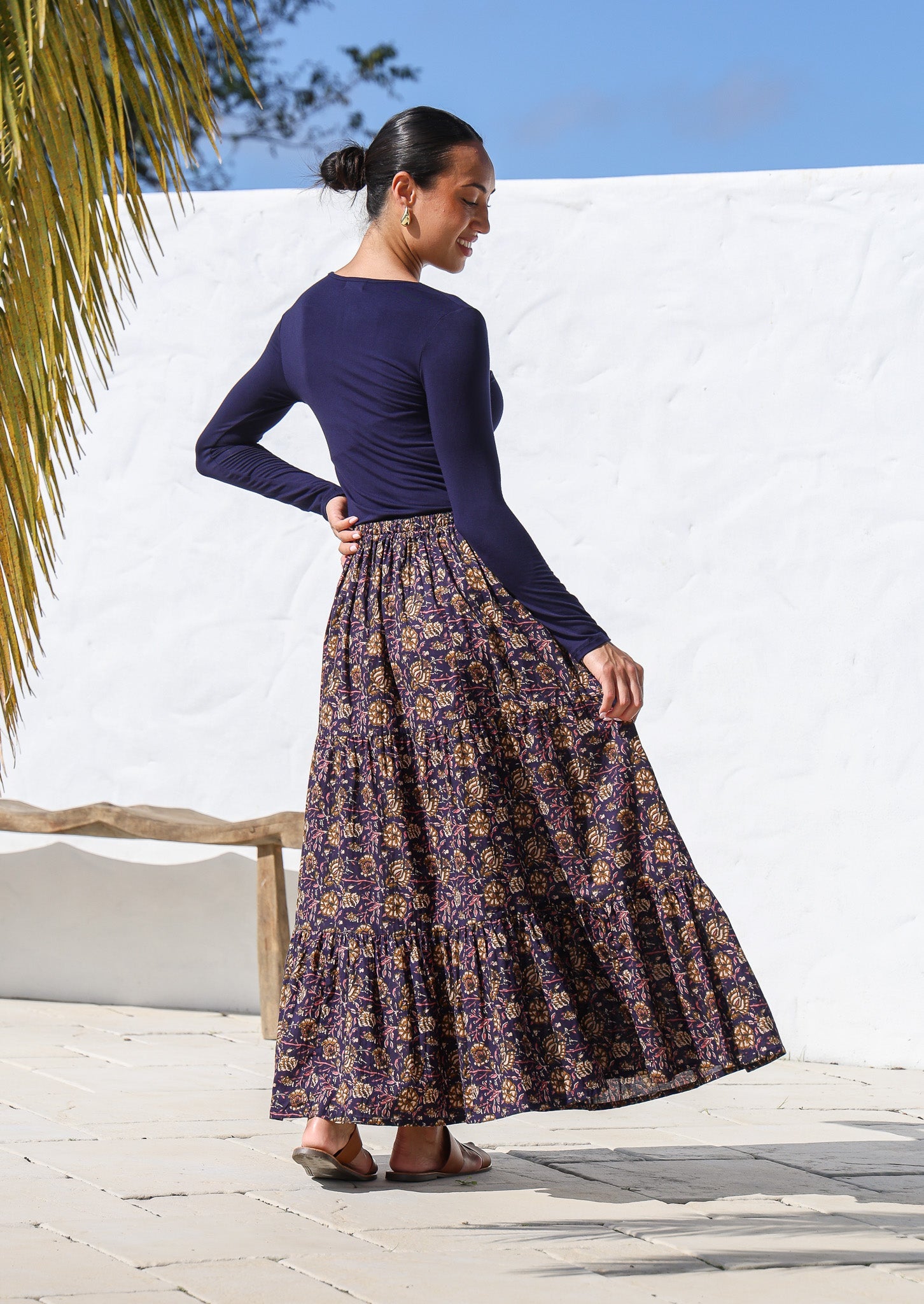 Model showcasing back of the cotton tiered maxi skirt in dark purple based sweet floral print.