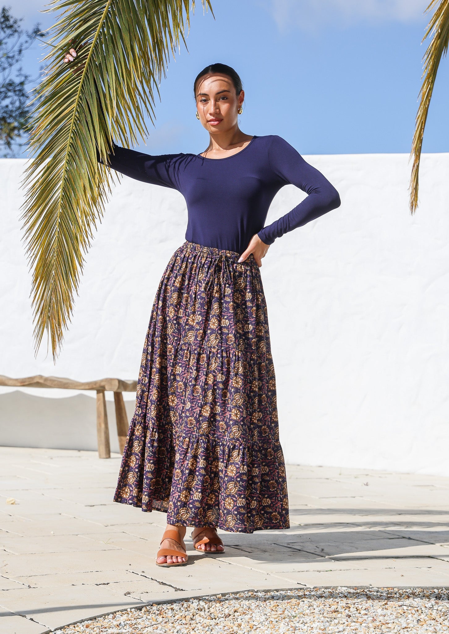 Woman wears cotton tiered maxi skirt with elastic waistband, drawstring and dark purple based floral print.