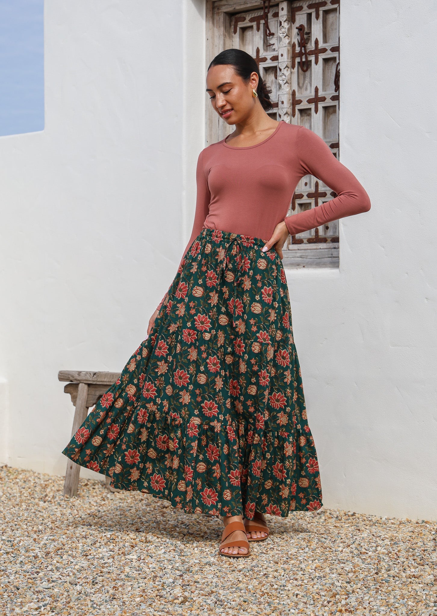 Model poses in 100% cotton maxi skirt with elasticised waist and drawstring in deep green based floral print.