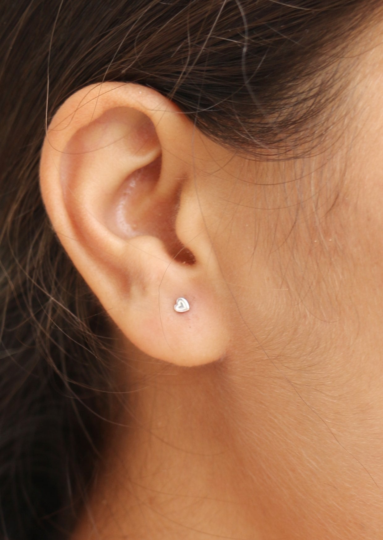 Close-up of an ear wearing a small silver heart stud with finely etched heart detail