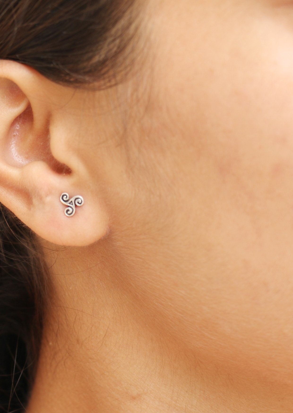Close-up of an ear wearing a small silver triskele studs with three spirals radiating from the center
