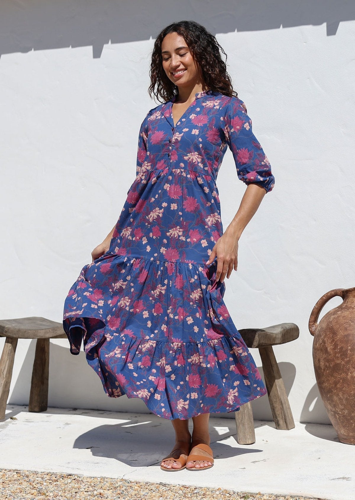 Model stands in sun wearing a navy blue 3/4 sleeved floral cotton maxi dress featuring burgundy, pale pink and plum florals