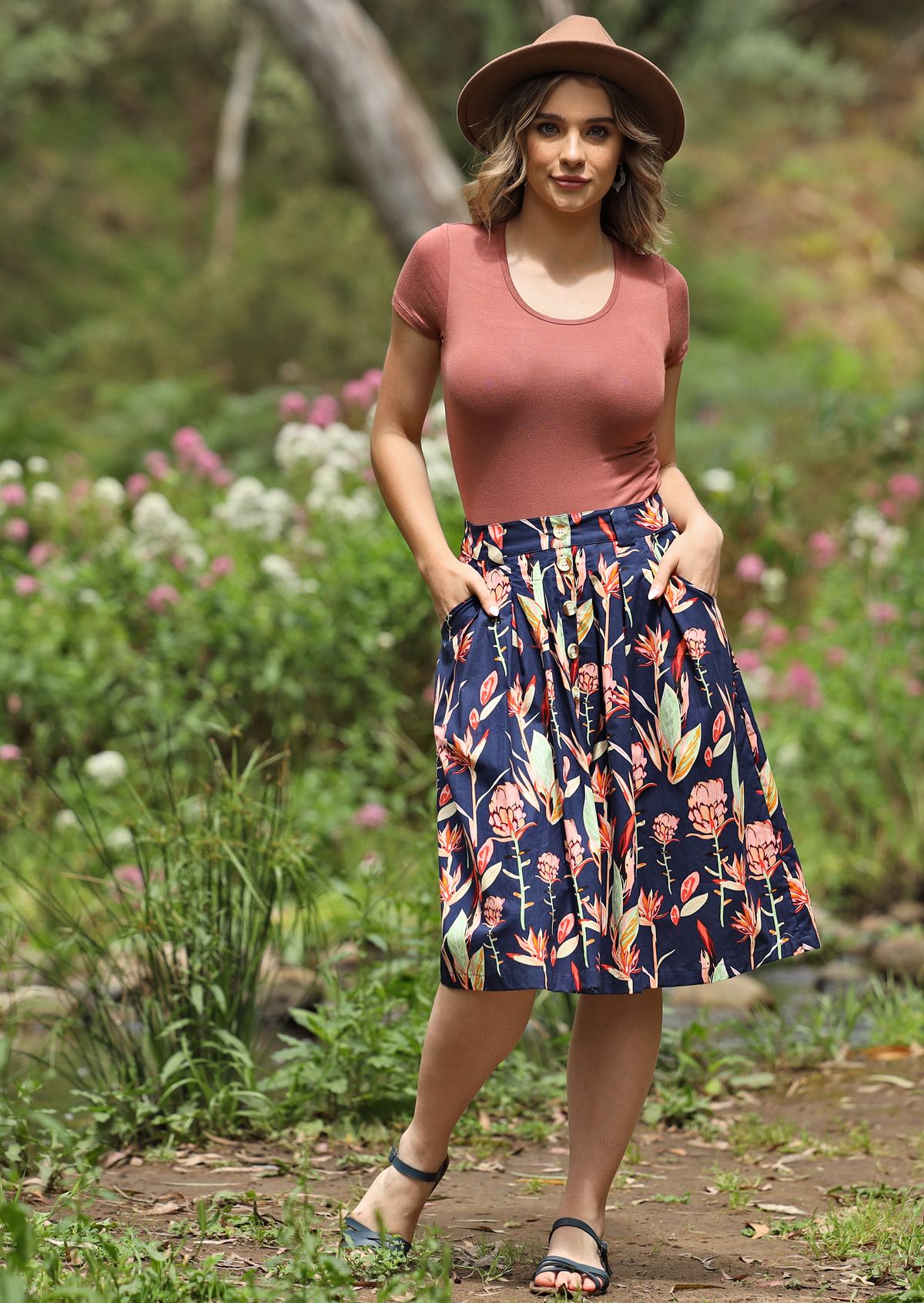 Model poses in cotton button through knee length skirt in botanical print paired with stretch rayon top, with hands in pockets