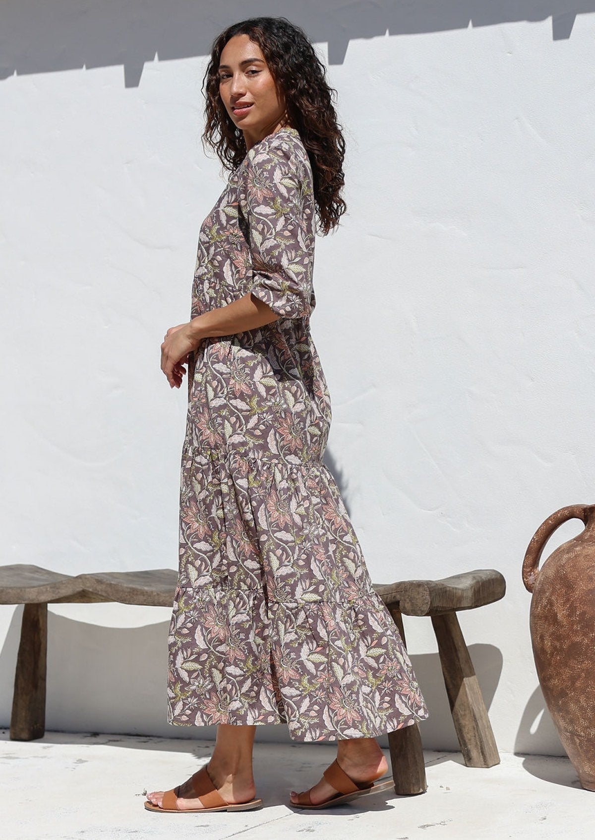 Woman standing in front of wooden bench wears three tiered cotton maxi dress with 3/4 sleeves, pockets and mandarin collar