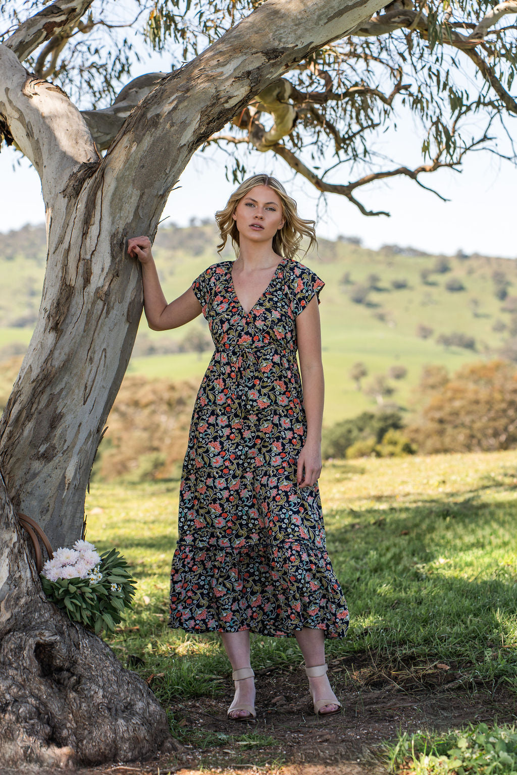 Model leaning on a tree wearing 100 percent rayon floral maxi dress