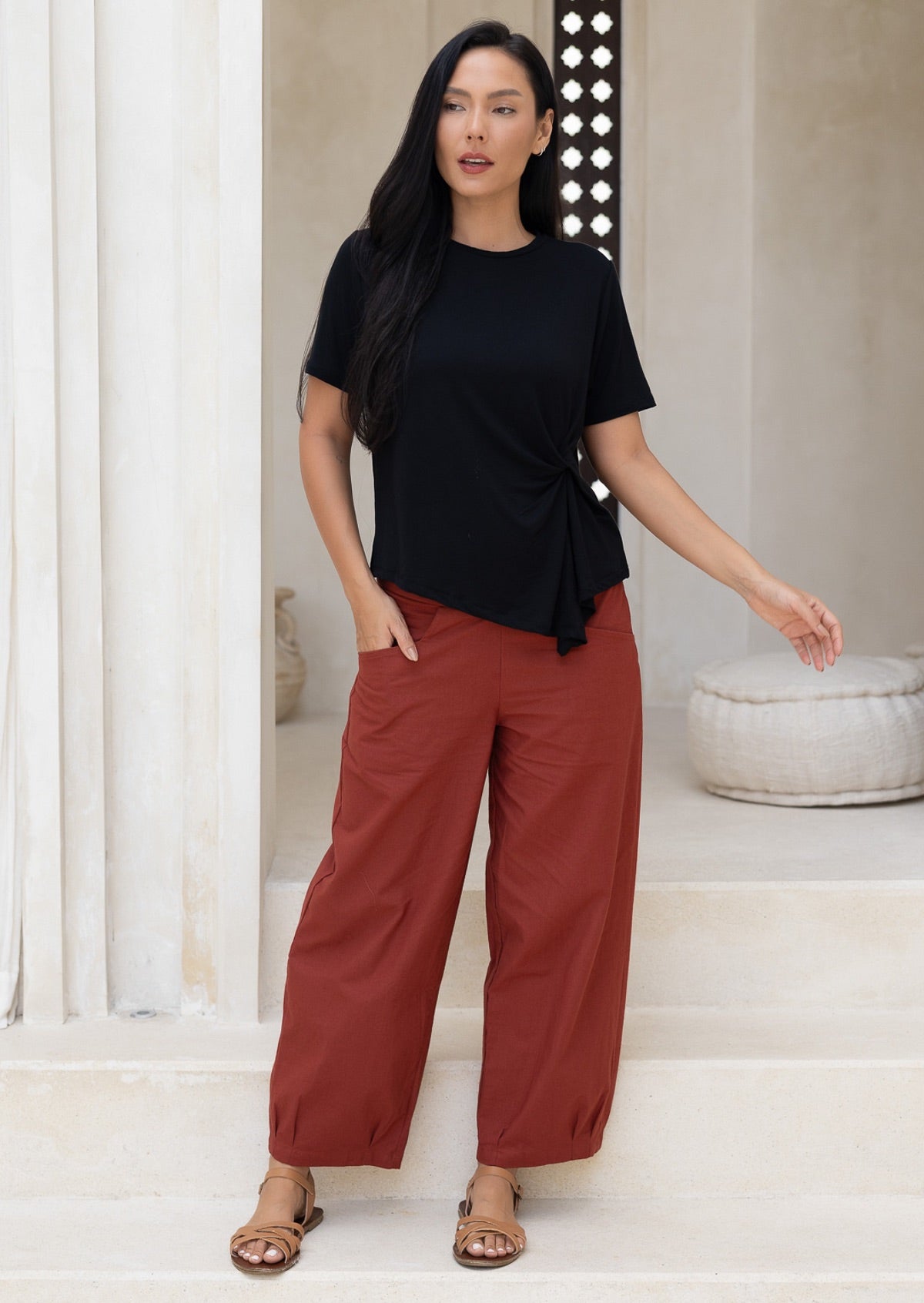 Model wears rust colour wide leg cotton pants with hand in pocket paired with basic black rayon top