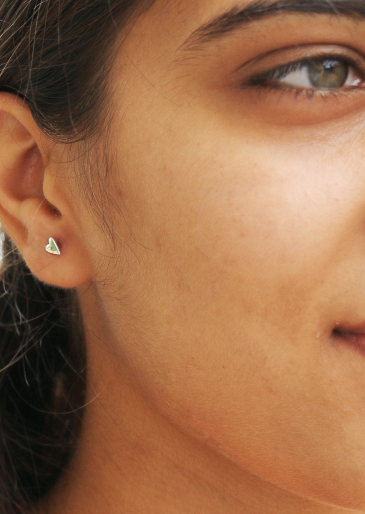 Woman with green eye wearing small sterling silver studs in elongated heart shape
