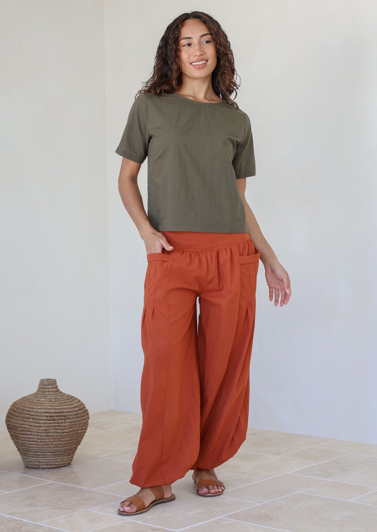 Woman wears relaxed fit lightweight rust shade cotton harem pants with pockets paired with a olive green top