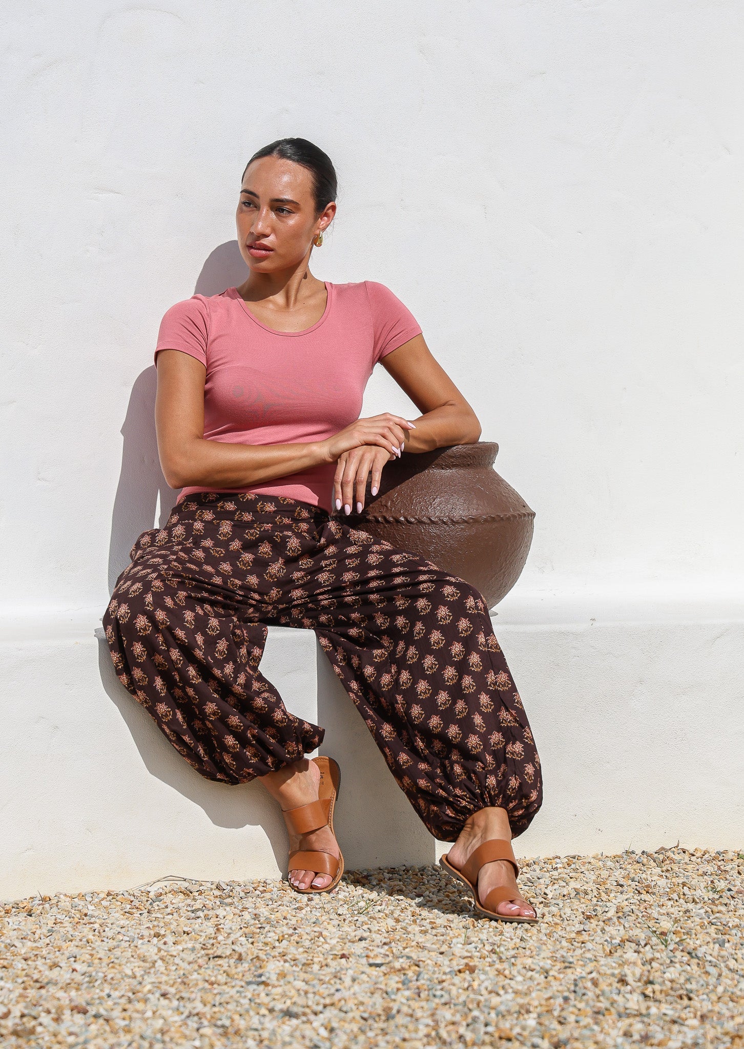 Model sitting on a bench wears 100% cotton harem pants with elasticated waist and ankles in brown based floral print.